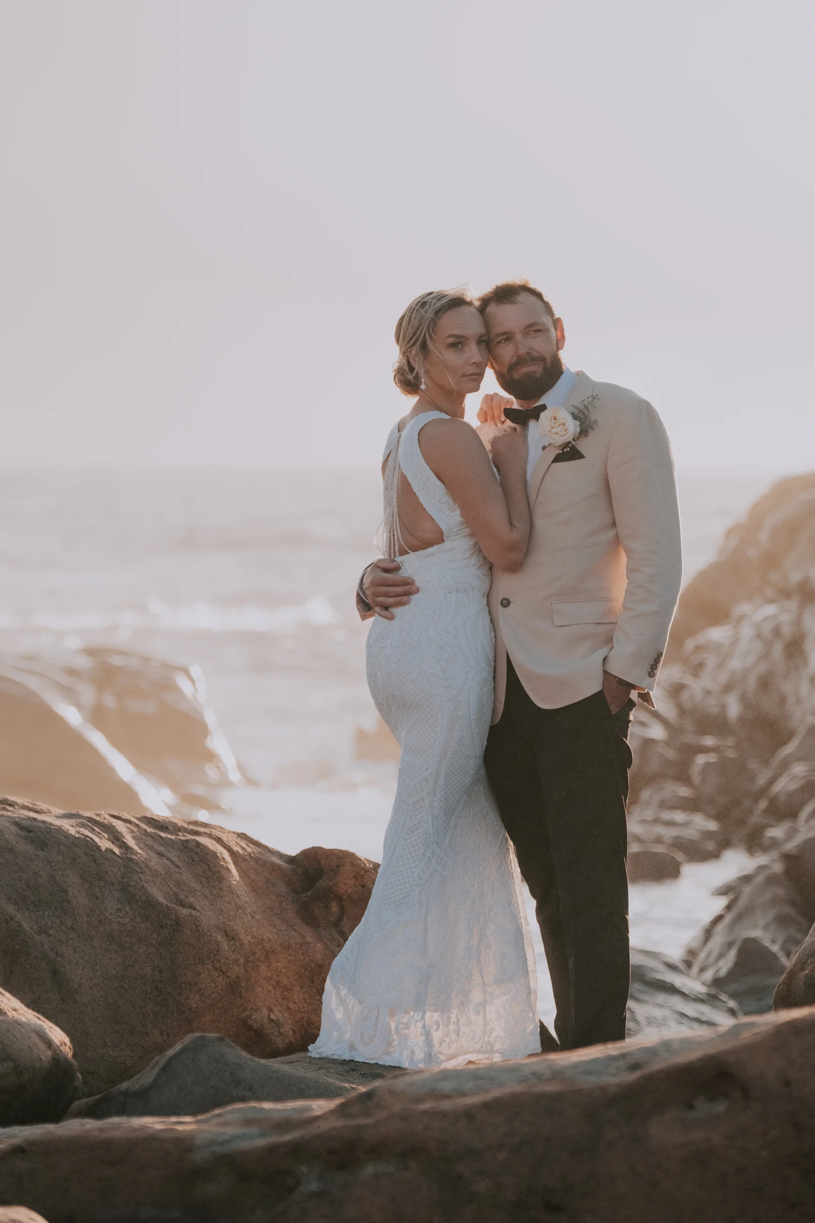Bride and groom embracing on the rocks at golden hour