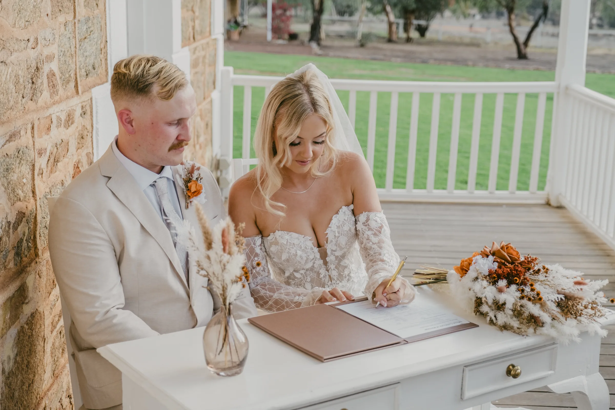 Grace and Lachie signing the marriage register on the verandah at Buckland Estate, wedding party gathered around