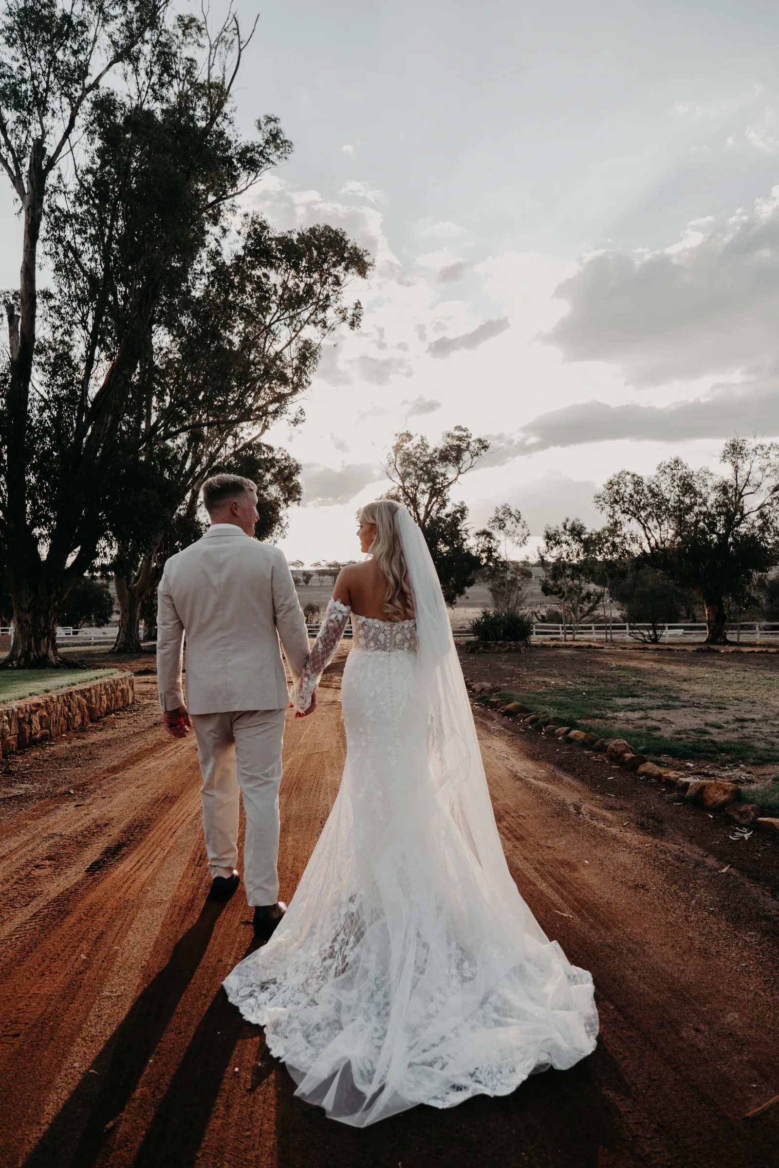 Grace's veil trailing in the wind as she and Lachie walk down the driveway at Buckland Estate