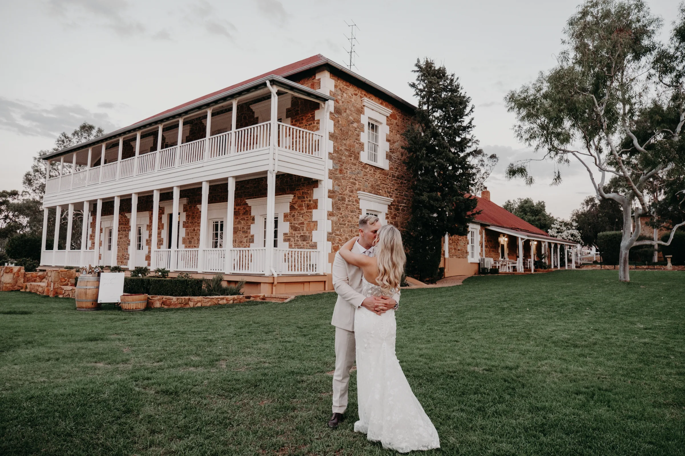 Wide shot of Grace and Lachie walking hand in hand with the Buckland Estate homestead glowing in the background