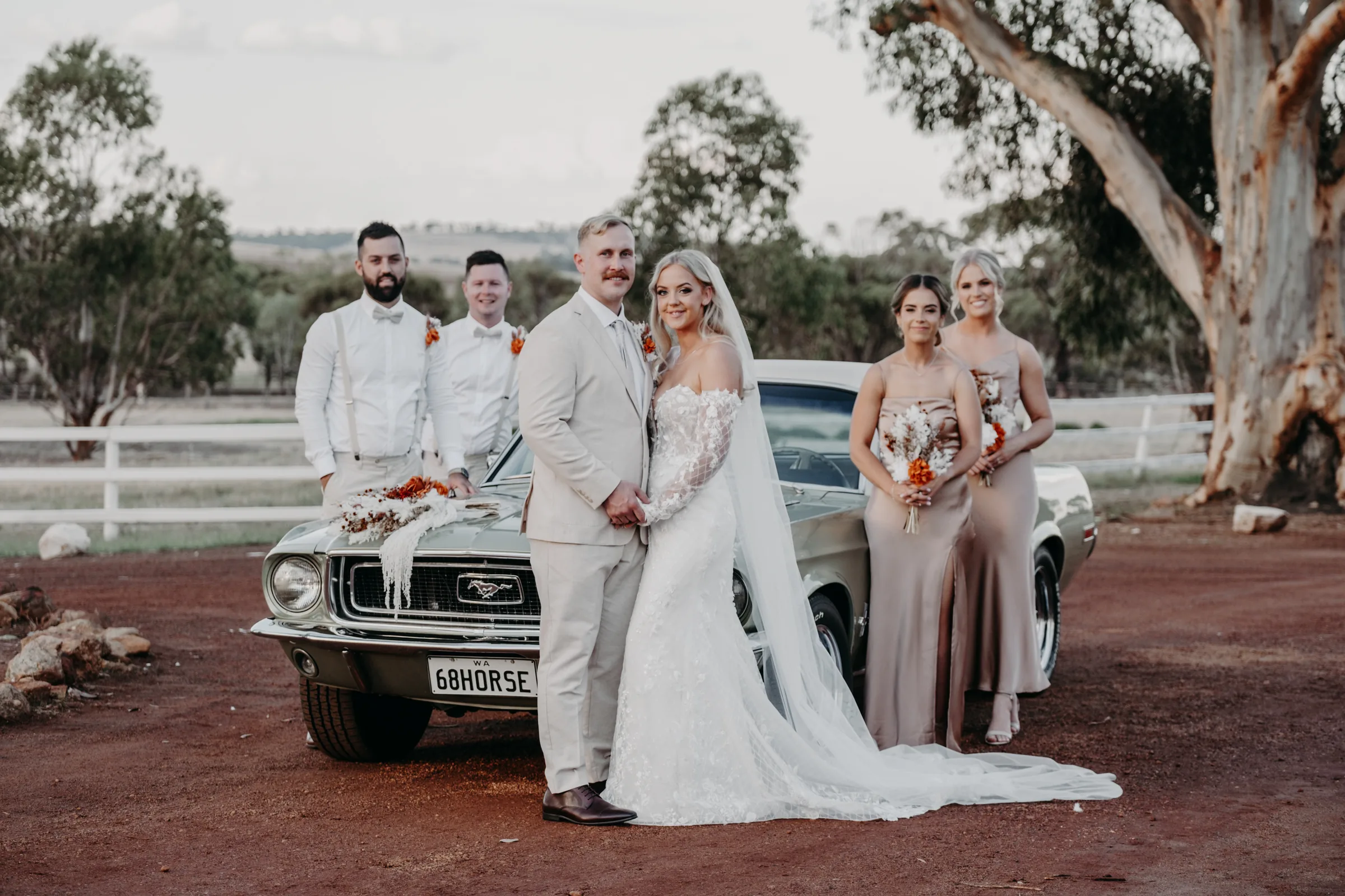 Grace and Lachie's wedding party gathered beside the vintage green muscle car on the red-dirt driveway at Buckland Estate