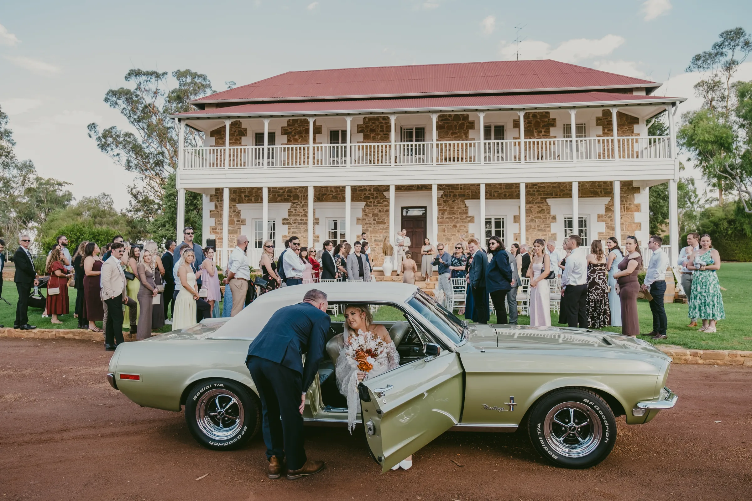 Wide view of Buckland Estate's homestead with guests gathering beside a vintage green car before the ceremony