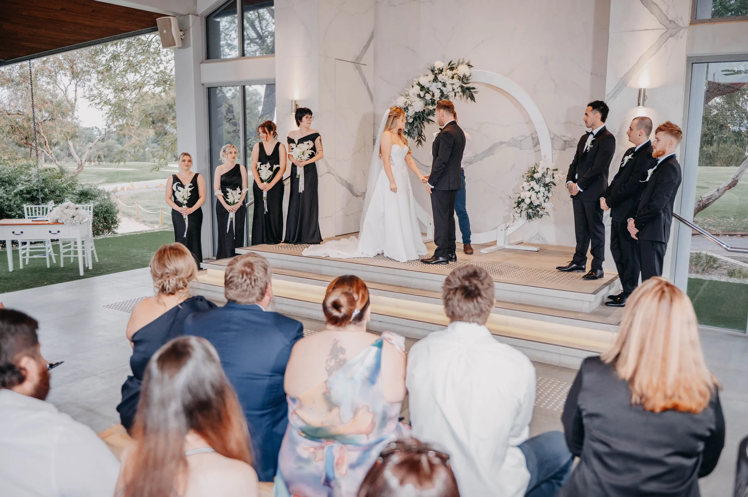 Wide symmetrical view of Kirra and Mitch exchanging vows beneath the arch at the Garden Pavilion