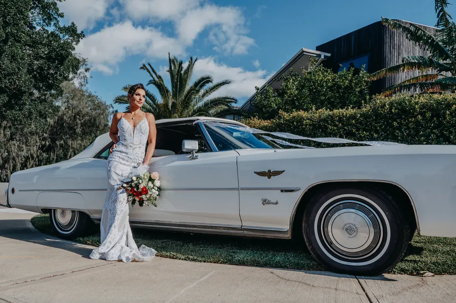 Full bridal party portrait leaning on the vintage Cadillac with the water behind them at sunset