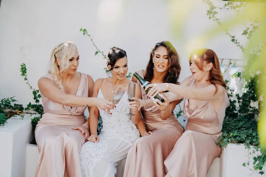 Bridal party laughing together around the vintage Cadillac in warm sunset light