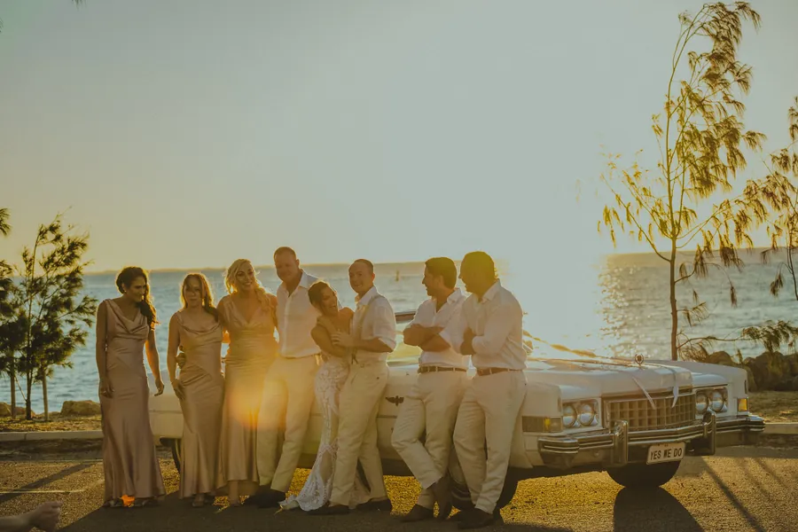 Katia standing beside the vintage Cadillac with her bouquet, palm trees and a home in the background