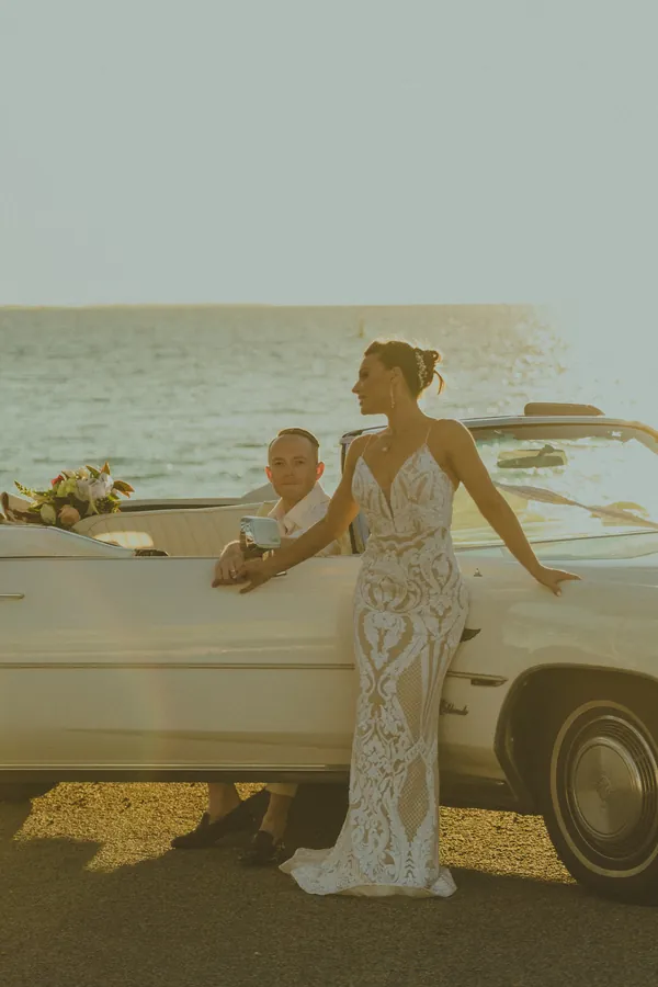 Katia standing beside the vintage Cadillac Eldorado, Sean seated inside, at golden hour