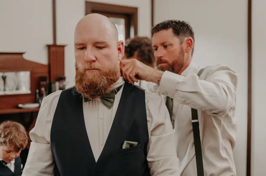 Close-up of a groomsman tying Ben's bow tie before the Dalmore Farm ceremony