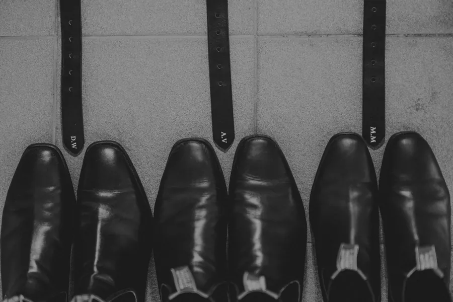 Detail shot of the groomsmen's polished dress shoes and monogrammed belts lined up before the ceremony