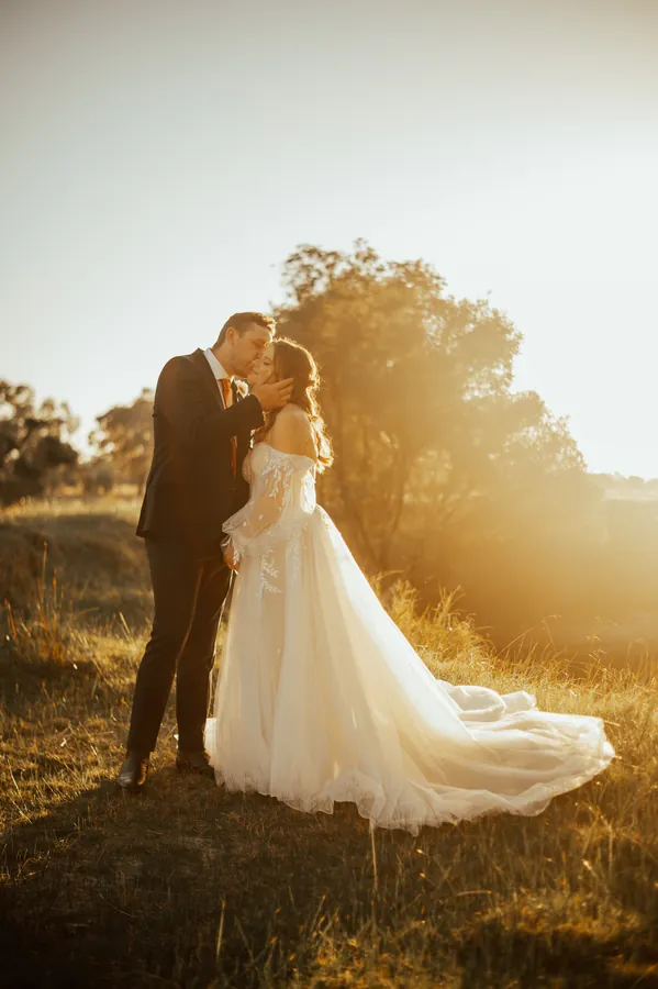 Groom kissing the bride's forehead in a golden sunlit field after their Hopeland wedding