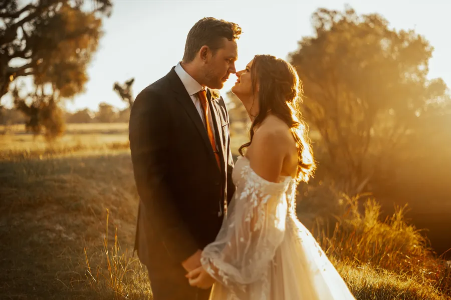 Bride and groom standing nose to nose about to kiss, lit by warm golden hour sun