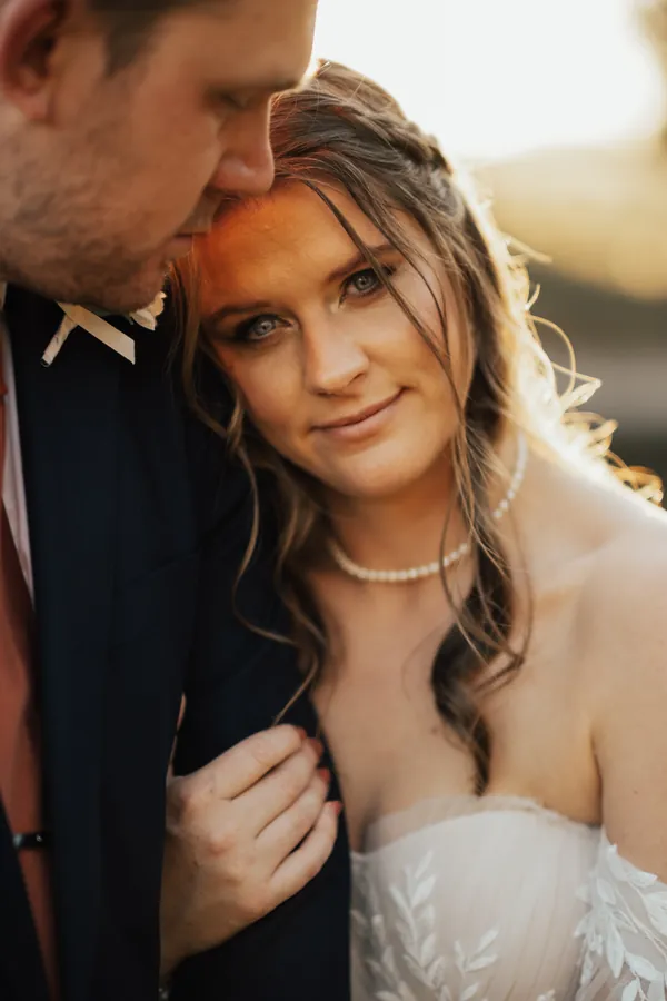Close portrait of the bride resting her head on the groom's shoulder at sunset
