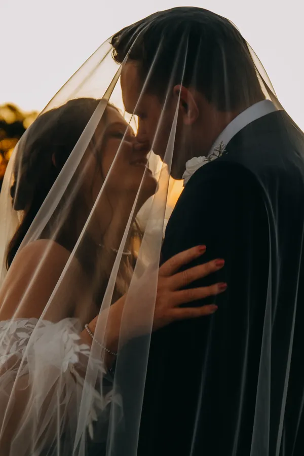 Bride resting her hand on the groom's chest under the veil, foreheads close together