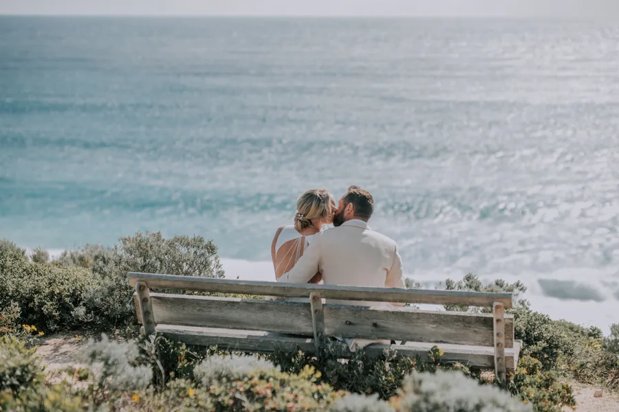 Victoria and Luck sitting together on a wooden bench, looking out over the ocean at Injidup Beach