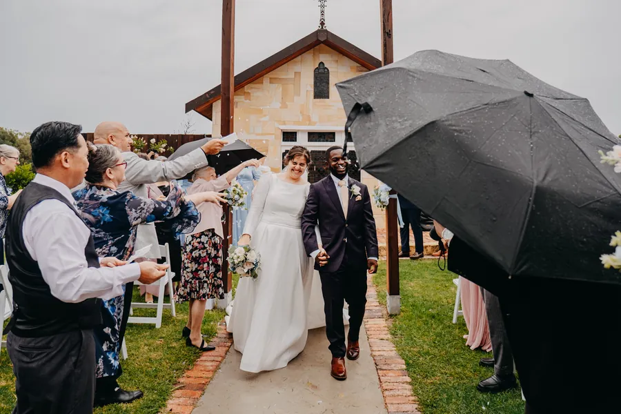 The celebrant sheltering under an umbrella mid-ceremony as rain falls over Chapel Farm Estate