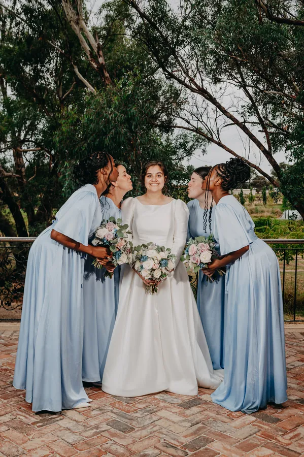 Bridesmaids kissing Cassandra's cheek in celebration at Chapel Farm Estate