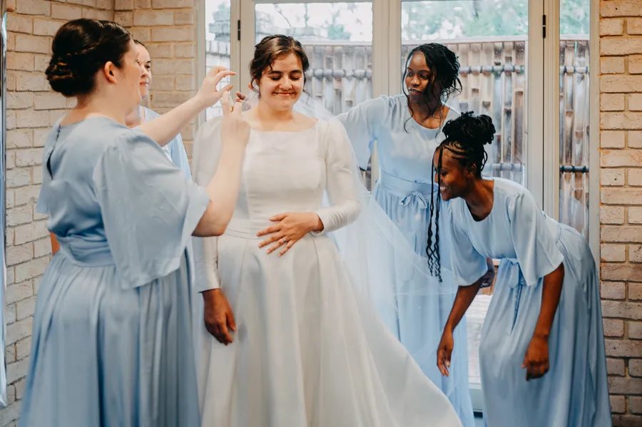 Bridesmaids in dusty blue gowns helping Cassandra into her wedding dress