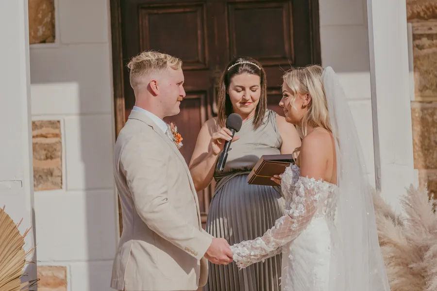 Lachie holding Grace's hands during their vows outside a timber door at Buckland Estate