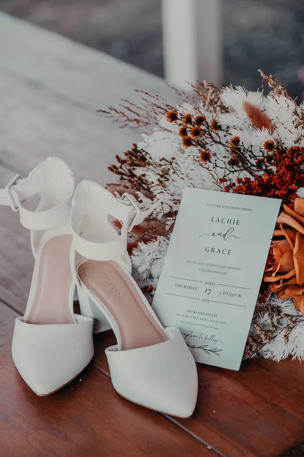 Bridal shoes and the wedding invitation suite styled on a timber table at Buckland Estate