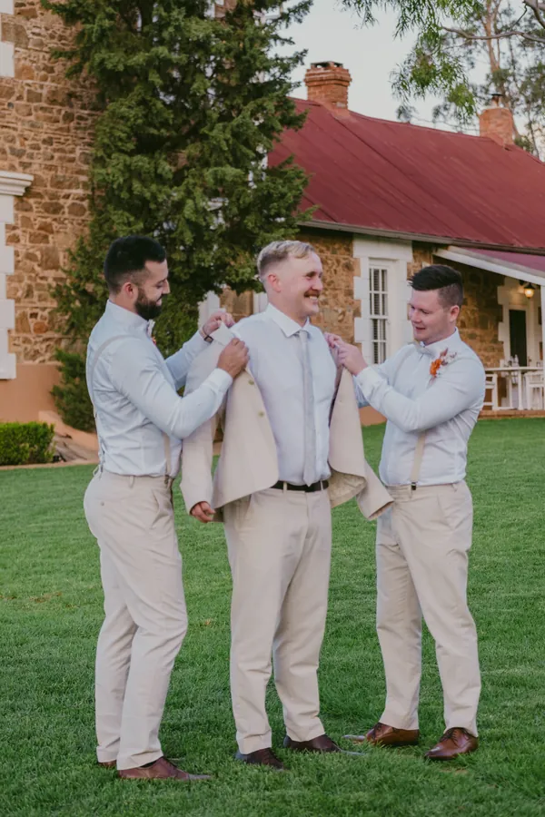 Groomsmen adjusting boutonnieres together in the sunshine before Grace and Lachie's ceremony