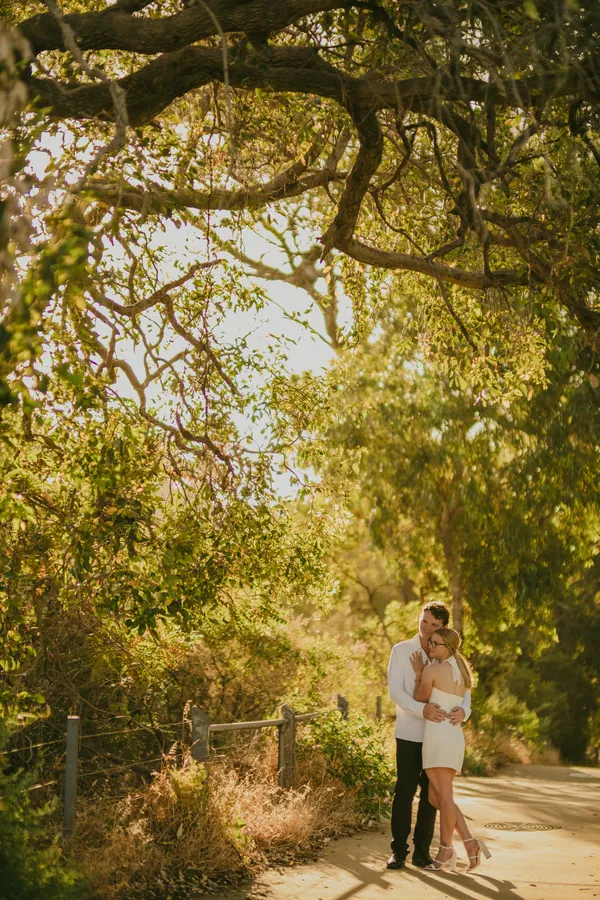 Kayla and Brett walking through a tree archway on a Kings Park pathway, seen from a distance