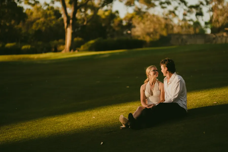 Wide shot of Kayla and Brett sitting together in an open field at Kings Park, golden hour light