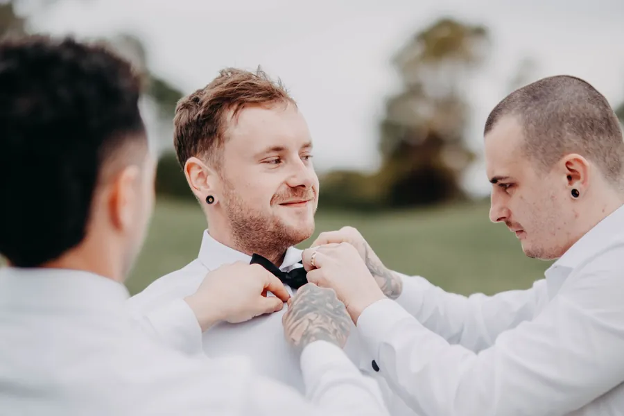 Close-up of a groomsman tying Mitch's bow tie before the wedding ceremony