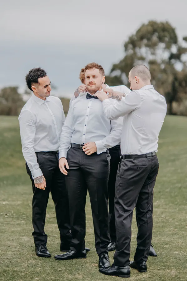 Mitch's groomsmen standing together adjusting bow ties on the lawn at The Vines Resort