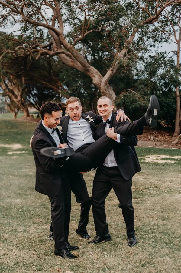 Groomsmen play-fighting on the fairway during Kirra and Mitch's wedding portraits