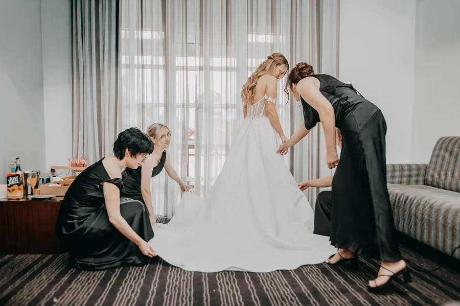 A bridesmaid helping Kirra into her wedding dress in the hotel room at The Vines Resort